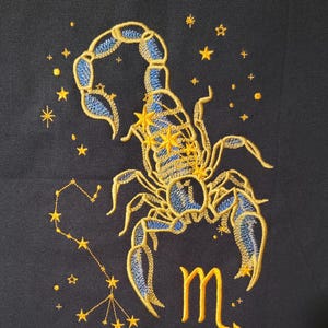 May include: Embroidered design of the Scorpio constellation, featuring a blue and gold scorpion with a gold 'M' symbol and a constellation of stars.