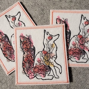 May include: Three white square patches with a fox design filled with pink, red, and yellow flowers. The fox outline is black, and the patches have a pink border. The patches are arranged at different angles.