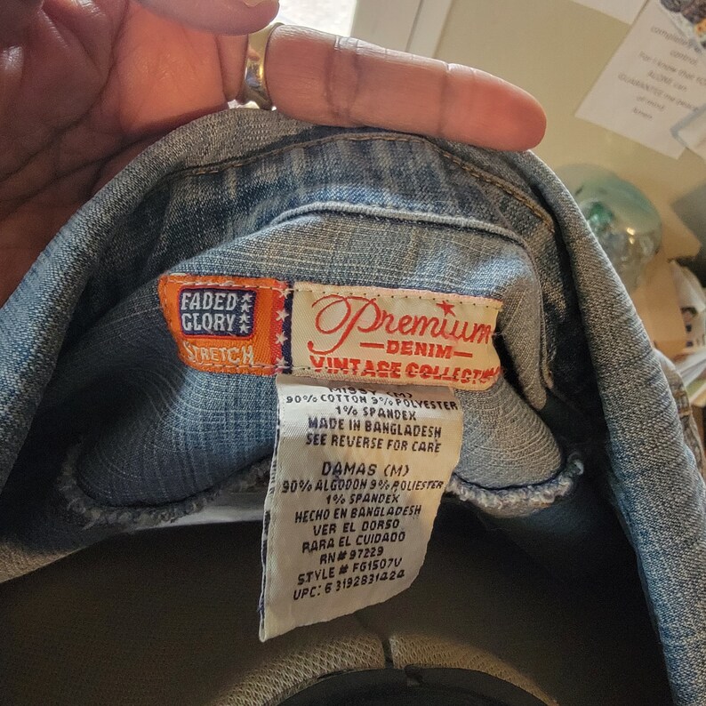 May include: A blue denim shirt with a red and white label that says "Faded Glory Stretch" and "Premium Denim Vintage Collection". The label also includes the fabric content and care instructions. The label says "90% Cotton 9% Polyester 1% Spandex", "Made in Bangladesh", "See reverse for care", "Damas (M)", "90% Algodon 9% Poli&eacute;ster 1% Spandex", "Hecho en Bangladesh", "Ver el dorso para el cuidado", "RN# 97229", "Style # FG1507V", "UPC: 6 3192831424".