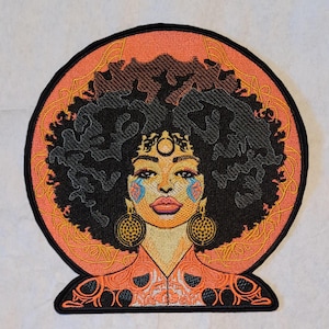 May include: Embroidered patch featuring a woman with dark curly hair and gold hoop earrings. The woman's face has colorful accents, and the patch is set against an orange background with gold filigree.