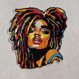 May include: Embroidered patch featuring a colorful portrait of a woman with dreadlocks. The artwork uses a vibrant palette of red, orange, yellow, blue, and white against a black background. The patch has a white border.