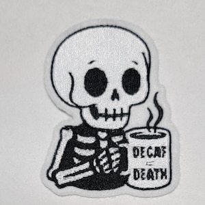 Puede incluir: Parche en blanco y negro con un esqueleto de dibujos animados sosteniendo una taza de café humeante. La taza dice "DECAF DEATH". El esqueleto tiene grandes cuencas de ojos negros y una expresión triste.