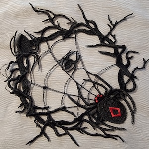 May include: Black spider web embroidery with a black spider in the center. The spider has red eyes and a red diamond on its abdomen.