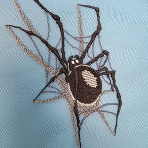 May include: Black embroidered spider with a web on a light blue background.