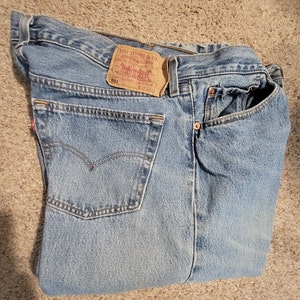 May include: A pair of blue denim jeans with a brown leather patch that reads "Levi Strauss & Co. Original  Quality Clothing" and "501" in white text.