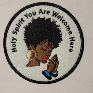 May include: A white round patch with black stitching around the edges. The patch has a black and white illustration of a woman with her hands clasped in prayer. The text "Holy Spirit You Are Welcome Here" is written in black around the woman's head.