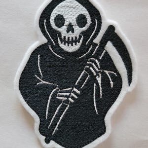 May include: Embroidered patch featuring a black Grim Reaper with a white skull and scythe. The patch has a white border and is designed with detailed stitching. Ideal for jackets, bags, or other fabric items.