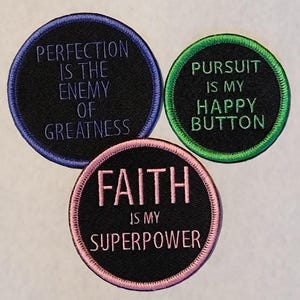 May include: Three embroidered patches with inspirational quotes. One patch reads "PERFECTION IS THE ENEMY OF GREATNESS" in purple on a black background with a blue border. Another says "PURSUIT IS MY HAPPY BUTTON" in green with a green border. The third says "FAITH IS MY SUPERPOWER" in pink with a pink border.