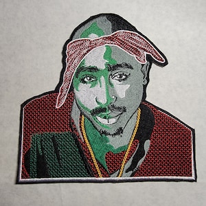 May include: Embroidered patch featuring a portrait of a rapper wearing a red bandana and a gold chain. The background is a red and green plaid pattern.