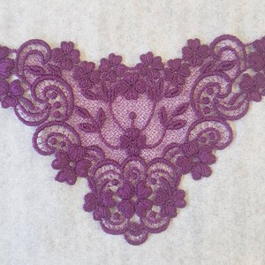 May include: Purple lace trim with a floral design. The lace is delicate and intricate, with a scalloped edge.