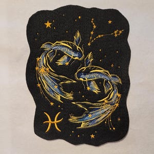May include: Embroidered patch with a black background and gold and blue stitching. The patch depicts the Pisces zodiac sign with two fish swimming in a circle. The constellation is also visible in the background.