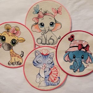May include: Four embroidered patches featuring cute animal designs. The patches are circular and have pink borders. The animals include a giraffe, an elephant, a cat, and another elephant. Each animal is wearing a pink bow and has large, expressive eyes.
