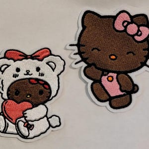 May include: Two embroidered patches featuring cartoon characters. One shows a brown character in a white bear costume holding a red heart. The other is a brown character with a pink bow and dress, waving.
