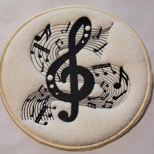 May include: A white round patch with a black treble clef and musical notes embroidered on it.
