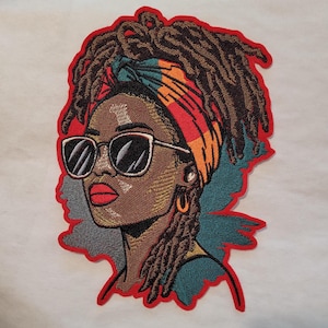 May include: Embroidered patch featuring a woman with brown skin, wearing sunglasses and a colorful headscarf. Her hair is styled in dreadlocks. The patch has a red outline.