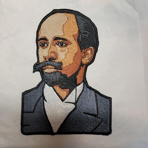 May include: Embroidered patch featuring a portrait of a man with a mustache and beard. The patch has a detailed design with shades of brown, black, and blue. The man is wearing a suit with a white shirt.