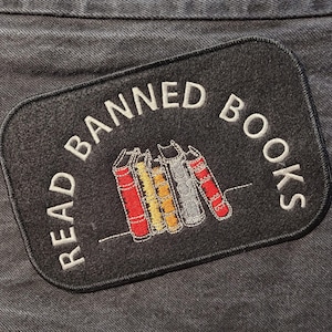 May include: Black fabric patch with white embroidery that reads "Read Banned Books". The patch features a row of five colorful books.