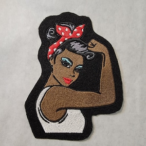 May include: Embroidered iron-on patch featuring a woman with brown skin, black hair, and red and white polka dot bandana. She is wearing a white tank top and has her arm raised in a 'We Can Do It' pose.