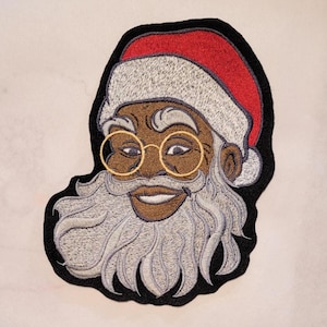 May include: Embroidered patch of a smiling Santa Claus with a white beard and mustache, wearing round gold-rimmed glasses and a red and white Santa hat.