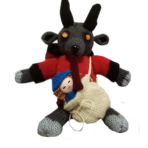 May include: A gray knitted goat with orange eyes wearing a red sweater and carrying a small knitted doll in a white bag.