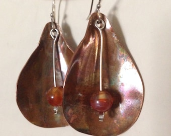 Organic shaped copper earrings with fire patina and carnelian bead drops hung on sterling ear wires.