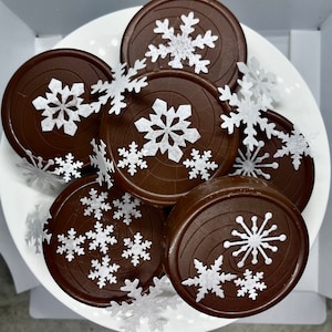 May include: A close-up of a plate of chocolate cookies decorated with white snowflake sprinkles. The cookies are arranged in a circle, with the snowflakes facing outwards.