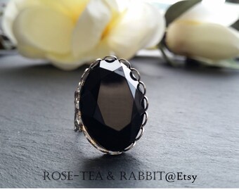 Puede incluir: Un anillo de piedra preciosa negra con engaste de plata. El anillo tiene un borde festoneado y una piedra preciosa grande y facetada.