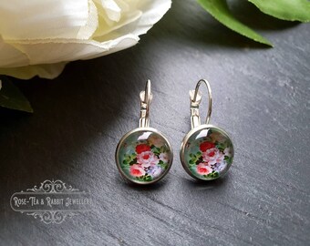 Puede incluir: Un par de pendientes de aro de plata con un diseño floral redondo. Los pendientes tienen un fondo azul claro con flores rosas, rojas y blancas.
