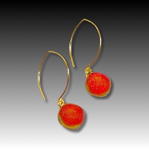 May include: A pair of gold dangle earrings with red and orange glass beads. The beads have a textured surface.
