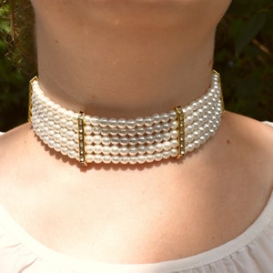May include: A white pearl choker necklace with gold accents. The necklace is made of multiple strands of pearls and has a clasp closure.