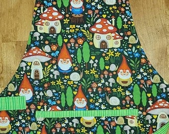 May include: A green and black apron with a gnome and mushroom pattern. The apron has a green and white striped trim and a large pocket.