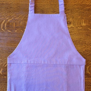 May include: A purple apron with white polka dots and adjustable straps. The apron has a large pocket in the front.