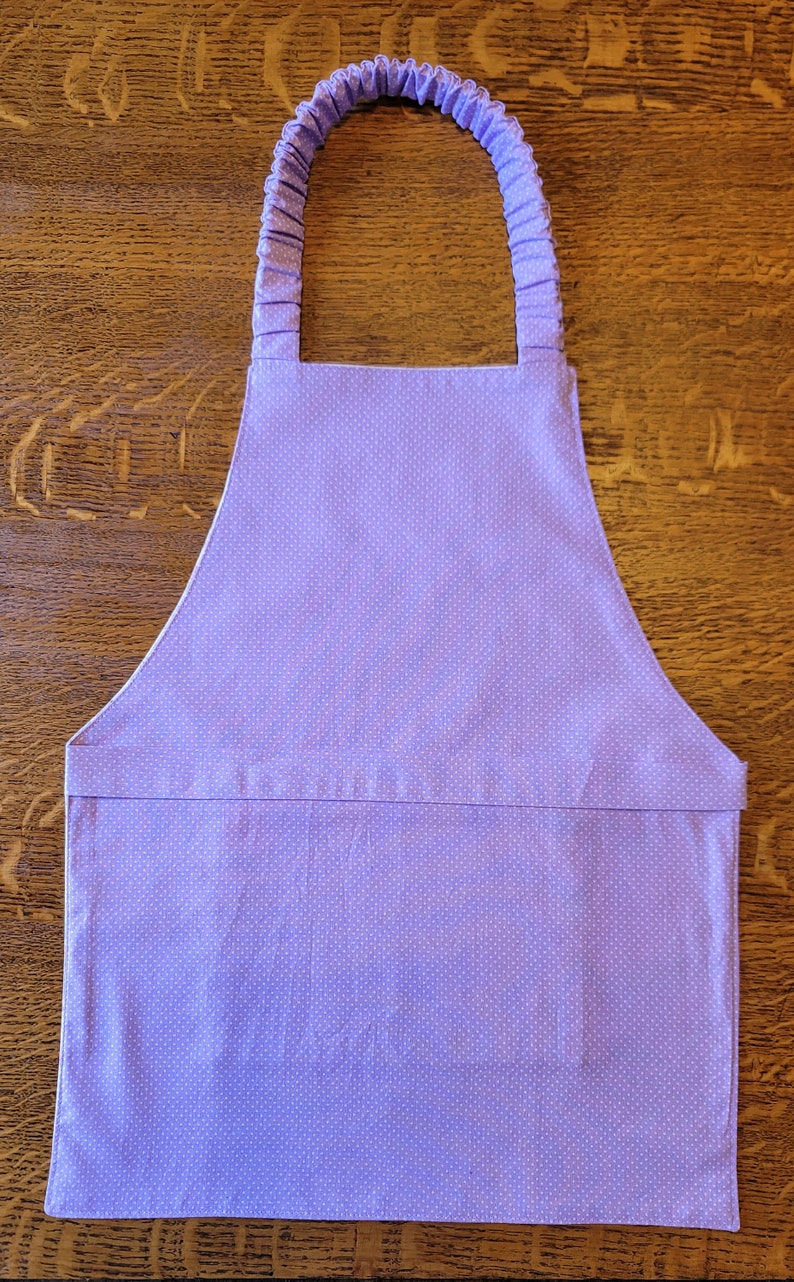 May include: A purple apron with white polka dots and adjustable straps. The apron has a large pocket in the front.