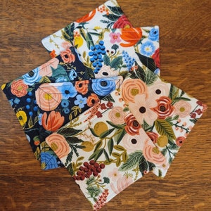 May include: Four fabric coasters with floral patterns. The coasters are made of a soft, quilted fabric and feature a variety of colors, including blue, green, red, and white.