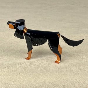May include: A stylized metal sculpture of a dog, primarily black with copper accents. The dog has a long body, a tail, and detailed legs. The sculpture is posed in a standing position, with its tongue slightly visible. The dog sculpture is a decorative item.