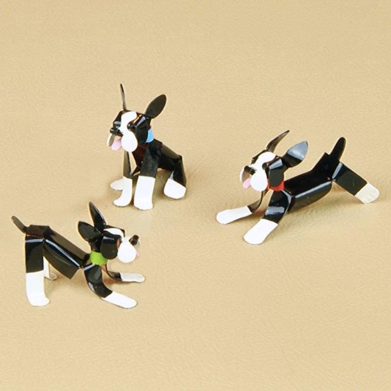May include: Three black and white metal Boston Terrier figurines. The figurines are in different poses, one sitting, one standing, and one running. The figurines are painted with black, white, and red accents.