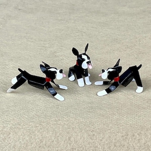 May include: Three black and white Boston Terrier figurines with red collars. The figurines are made of metal and are posed in different positions.