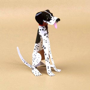 Puede incluir: Una figurita de perro de papel, de color blanco y negro con manchas, con un collar rojo. El perro está sentado con la lengua fuera.
