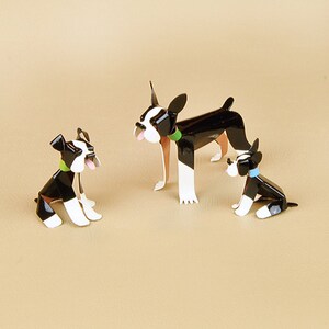May include: Three black and white Boston Terrier dog figurines. The largest figurine is standing with its tongue sticking out. The two smaller figurines are sitting. All three figurines have green and blue collars.