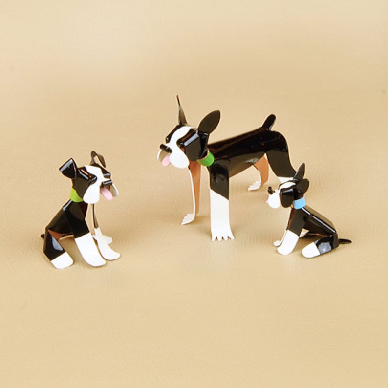 May include: Three black and white Boston Terrier dog figurines. The largest figurine is standing with its tongue sticking out. The two smaller figurines are sitting. All three figurines have green and blue collars.
