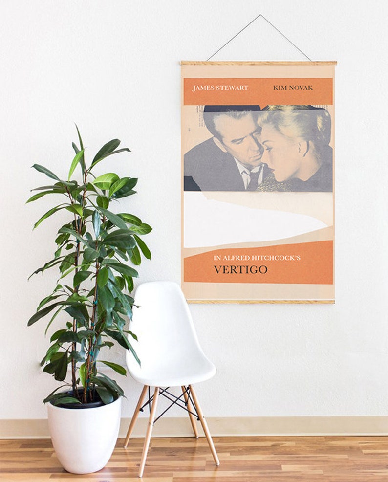 Puede incluir: Un p&oacute;ster enmarcado de la pel&iacute;cula "Vertigo" de Alfred Hitchcock con James Stewart y Kim Novak. El p&oacute;ster tiene un dise&ntilde;o vintage con tonos naranja y beige. Una silla blanca y una planta en maceta est&aacute;n en primer plano.