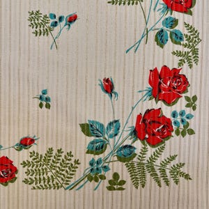 May include: A cream-colored fabric featuring a repeating pattern of vibrant red roses, teal-colored leaves, and green fern-like foliage. The background is textured with thin, vertical metallic gold stripes running throughout the entire material.