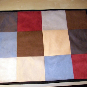 May include: A patchwork quilt with a black border. The quilt is made of nine squares of different colors, including brown, red, beige, and blue.