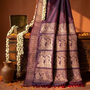 May include: A deep purple fabric drape featuring intricate gold-toned woven patterns of figures standing under trees. The textile includes a wide decorative border with detailed motifs and a fringe edge at the bottom, showcasing a rich colour palette.