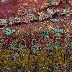 May include: A deep magenta and metallic gold fabric featuring intricate embroidery, silver sequins, and three-dimensional light blue fabric flower appliqués. The textile displays a complex pattern of swirling lines and decorative beadwork throughout.