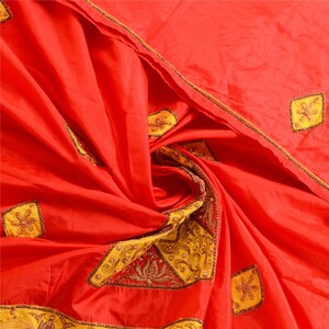 May include: A vibrant red fabric featuring a series of yellow diamond-shaped patches. Each yellow patch is adorned with intricate gold-toned embroidery, including floral motifs and swirling patterns, creating a textured and decorative appearance.