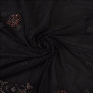 May include: Black sheer fabric with embroidered floral details. The fabric is draped and features a repeating floral pattern along the edges and scattered across the surface. Some of the floral details are embellished with sequins.