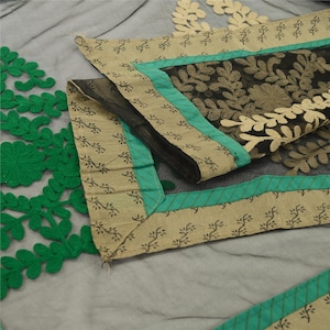 May include: A close-up of a black and green fabric with embroidered floral designs. The fabric has a beige border with a green and white trim.