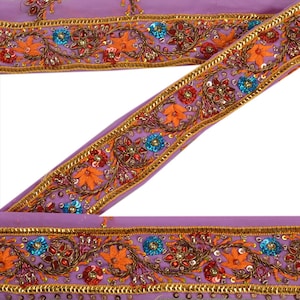 Puede incluir: Primer plano de una cinta decorativa morada con bordados intrincados. La cinta presenta diseños florales naranjas y rojos, lentejuelas azules y ribetes dorados. Ideal para proyectos de manualidades y costura.