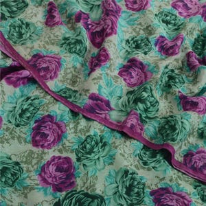 May include: A close-up of a fabric with a floral pattern. The fabric is a light green color with a white background. The flowers are a dark green and purple color.